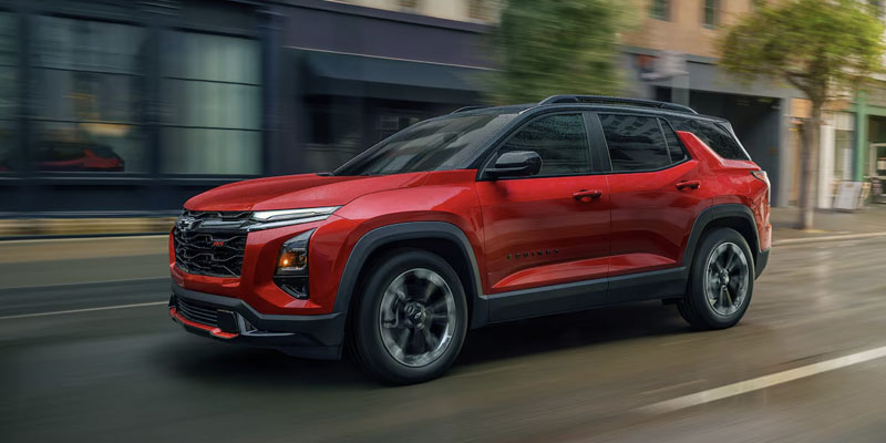 Front drivers side view of a red 2025 Chevy Equinox driving down a city street on a rainy day