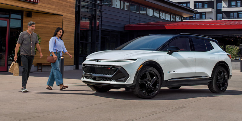 A couple walking toward the front passenger side of a white 2-025 Chevy Equinox EV parked on a city street during the daytime